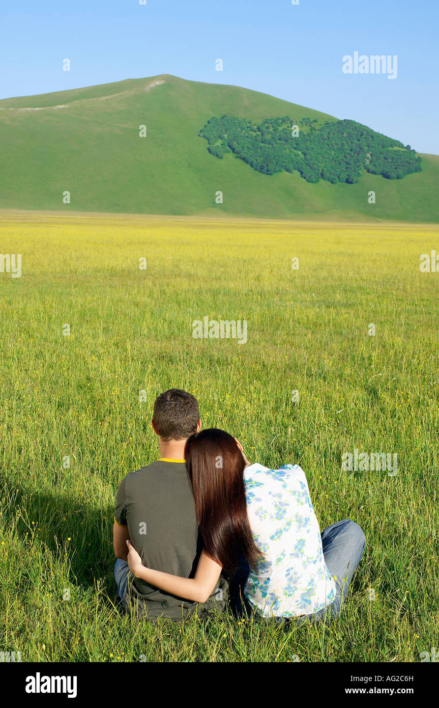 Young couple sitting in mountain field, back view Stock Photo - Alamy