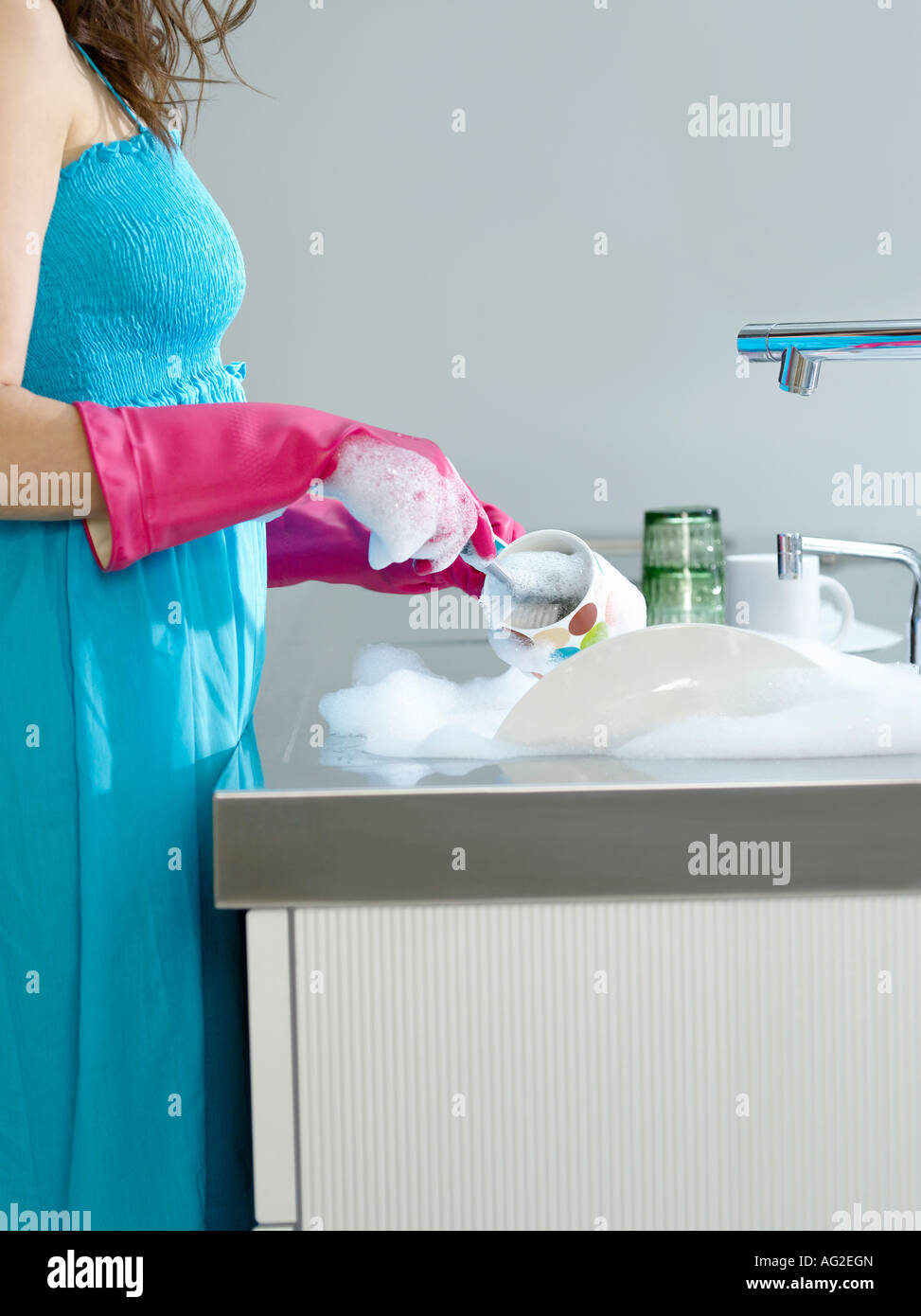 Woman wearing dress and rubber gloves, washing dishes, side view, mid