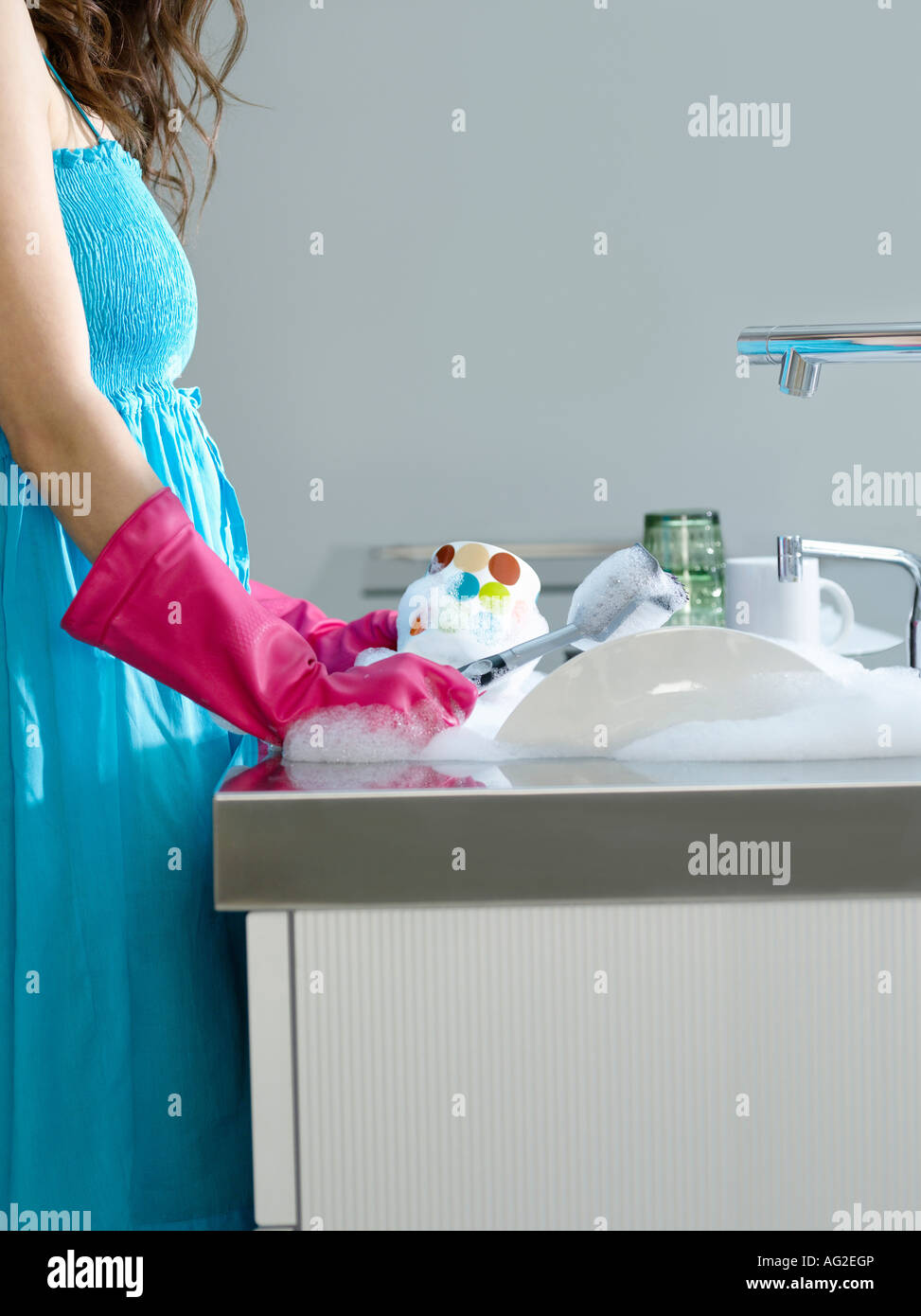 Woman wearing dress and rubber gloves, washing dishes, side view, mid