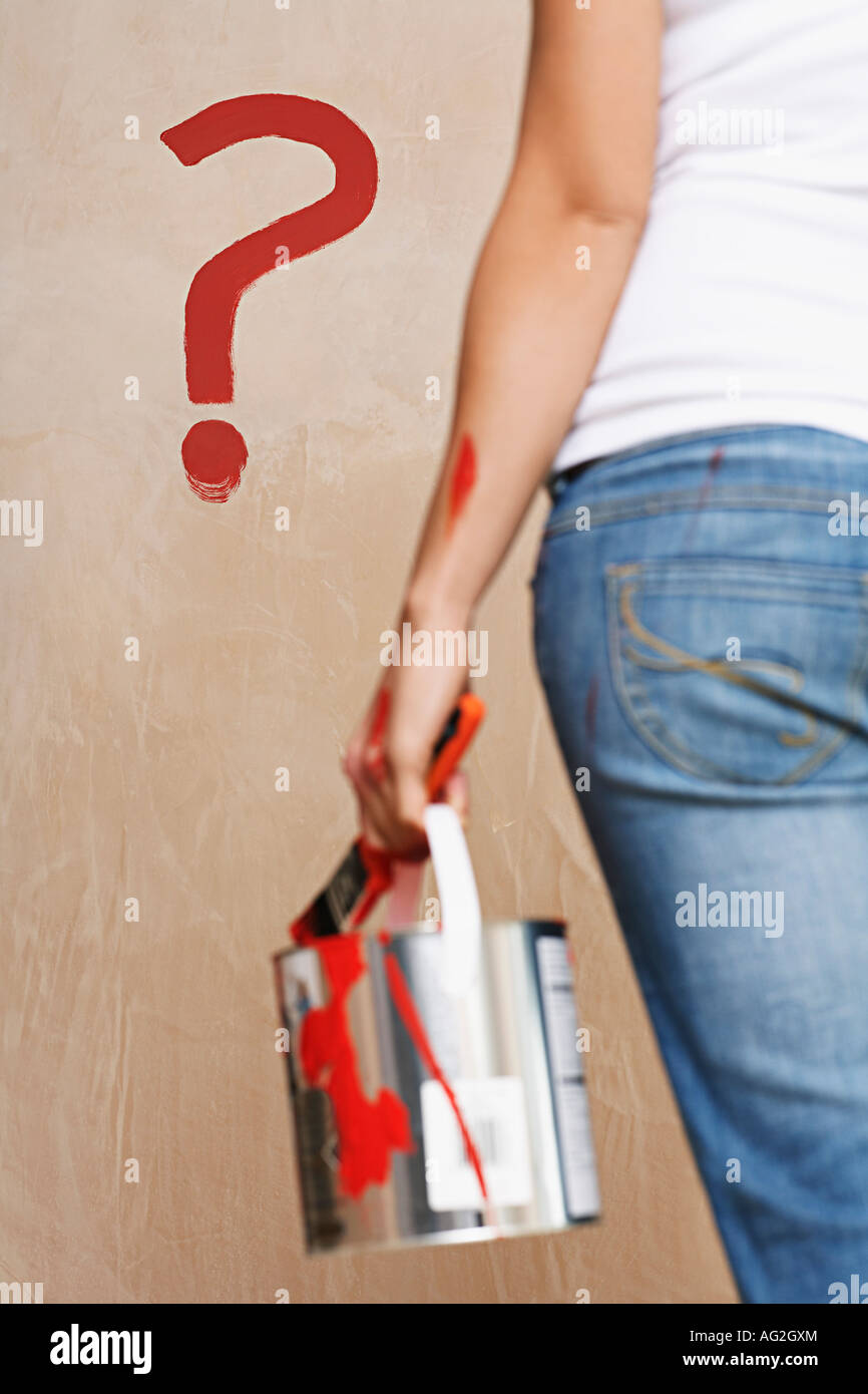 Woman holding painting can facing wall with painted question mark, mid