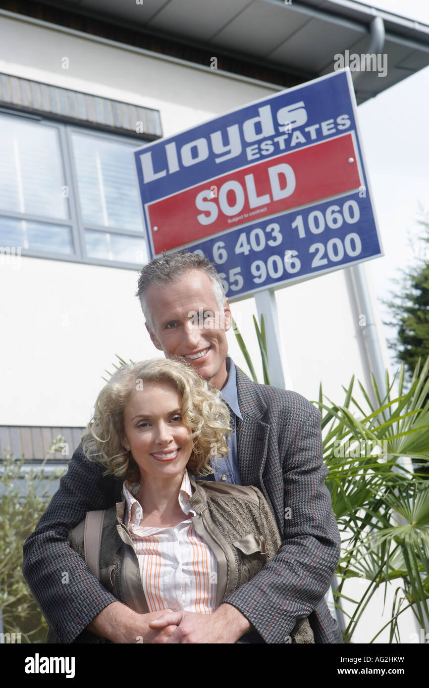 Couple embracing outside new home with sold sign, portrait Stock Photo ...