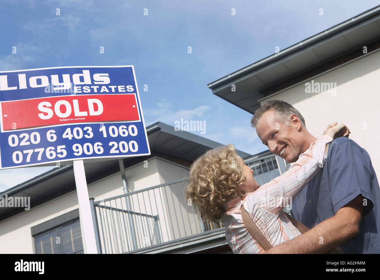 Couple embracing outside new home with sold sign Stock Photo - Alamy