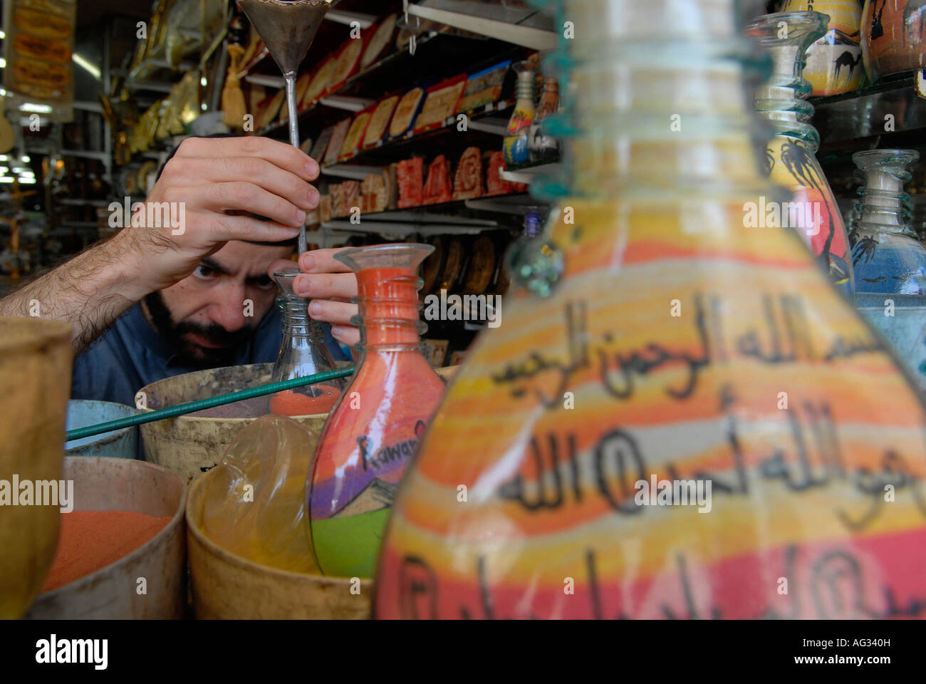 Jordanian man adds colored sand to a decorated bottle filled with multicolored sand rocks that is found in Petra in a souvenir shop in Amman Jordan Stock Photo