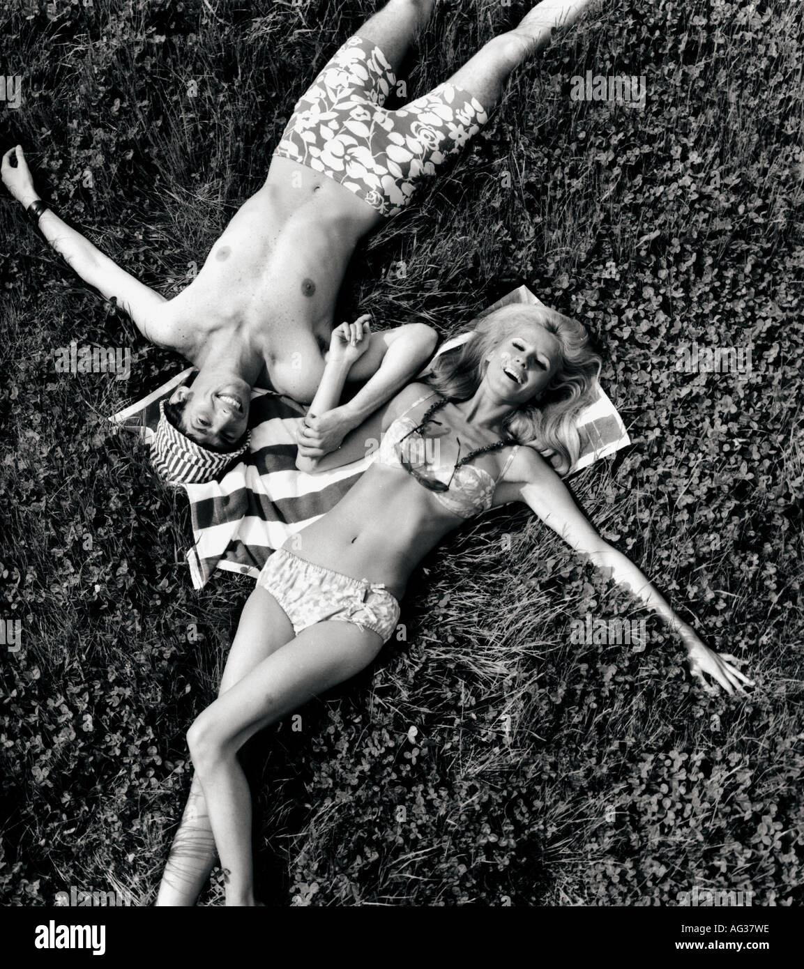 fashion, couple, lying in meadow, full length, 1960s, 60s, bikini, trunks, bathing suit, clothing, two-piece, sunglasses, accessory, Hawaiian, Hawaii, pattern, patterned, flower, flowers, bow, towel, hat, sun shade, , Stock Photo