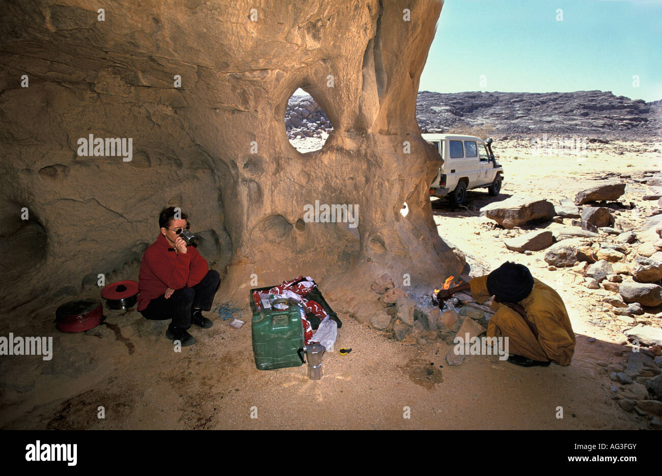 Algeria near Tamanrasset Tourist having lunch with man of Tuareg tribe sitting beside fireplace Stock Photo