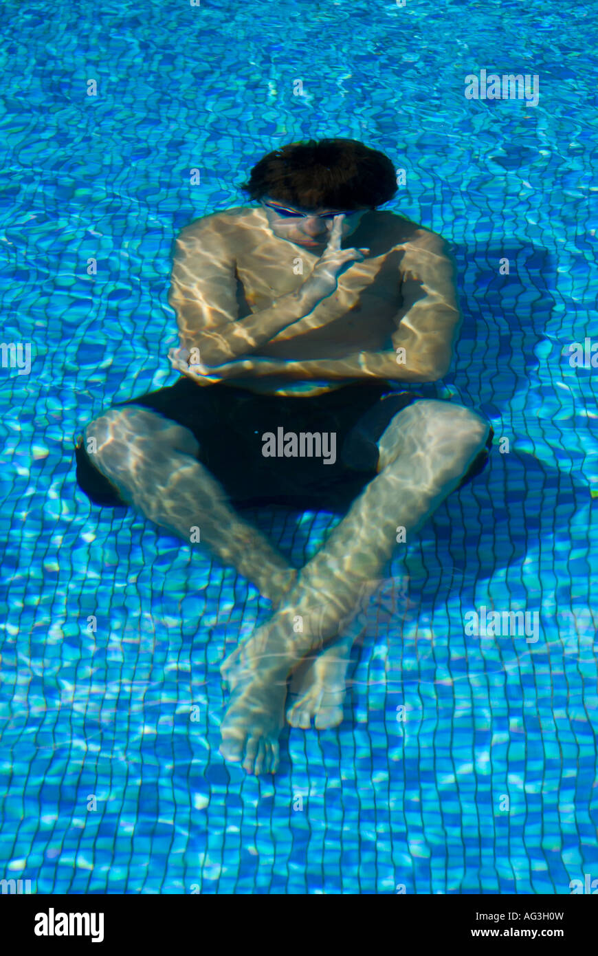 Teenager boy sitting at the bottom of the pool with a blessing hand