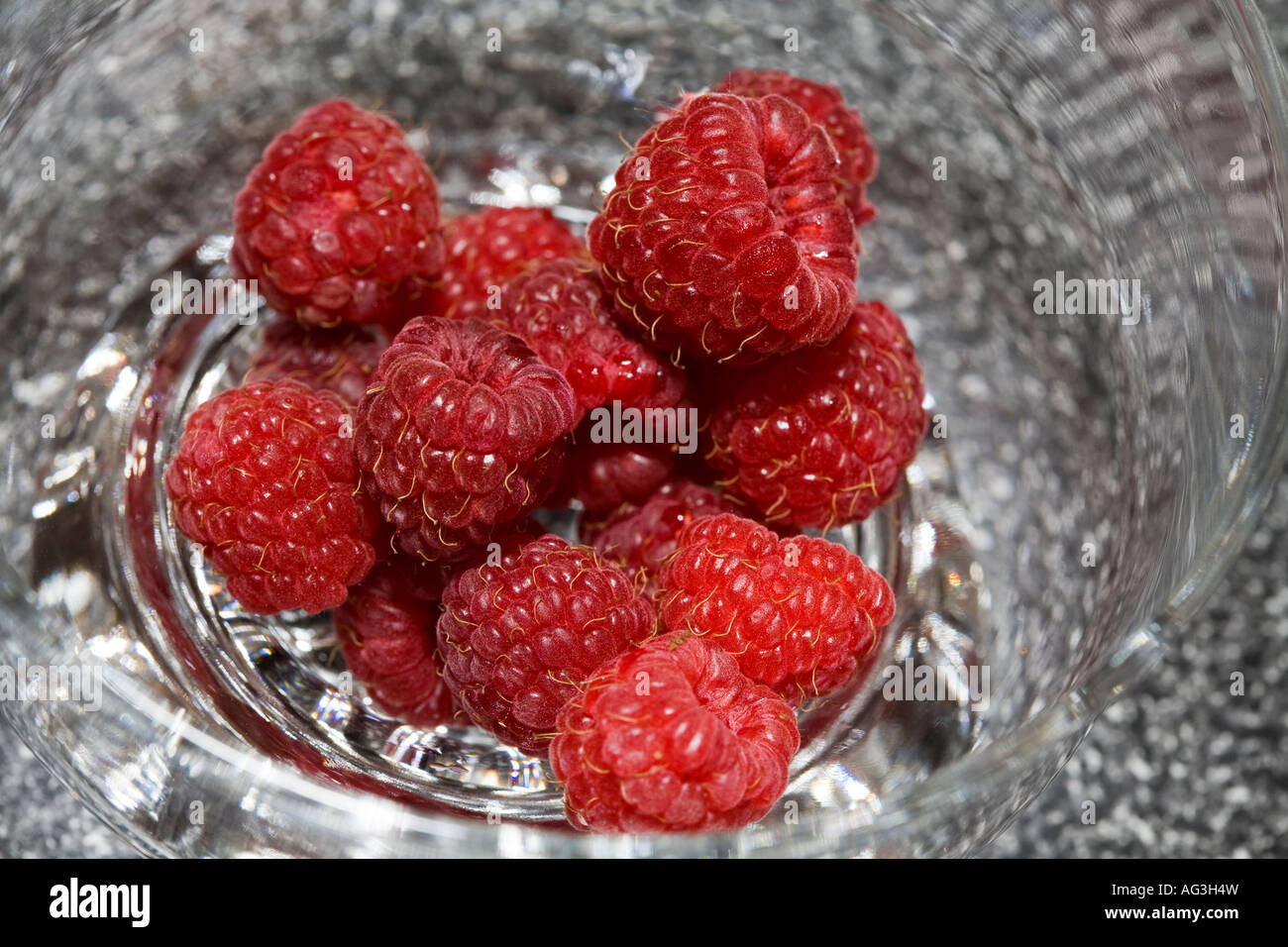 A Bowl of Red Raspberries A close up shot of a glass bowl of fresh plump red ripe raspberries against a grey background Stock Photo