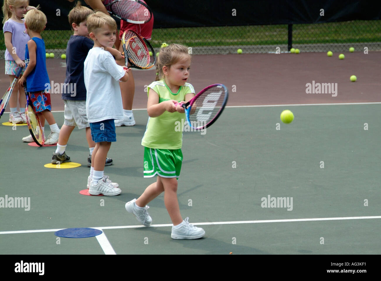 4 and 5 year old children take group tennis lessons taught by college students at a public tennis court Stock Photo