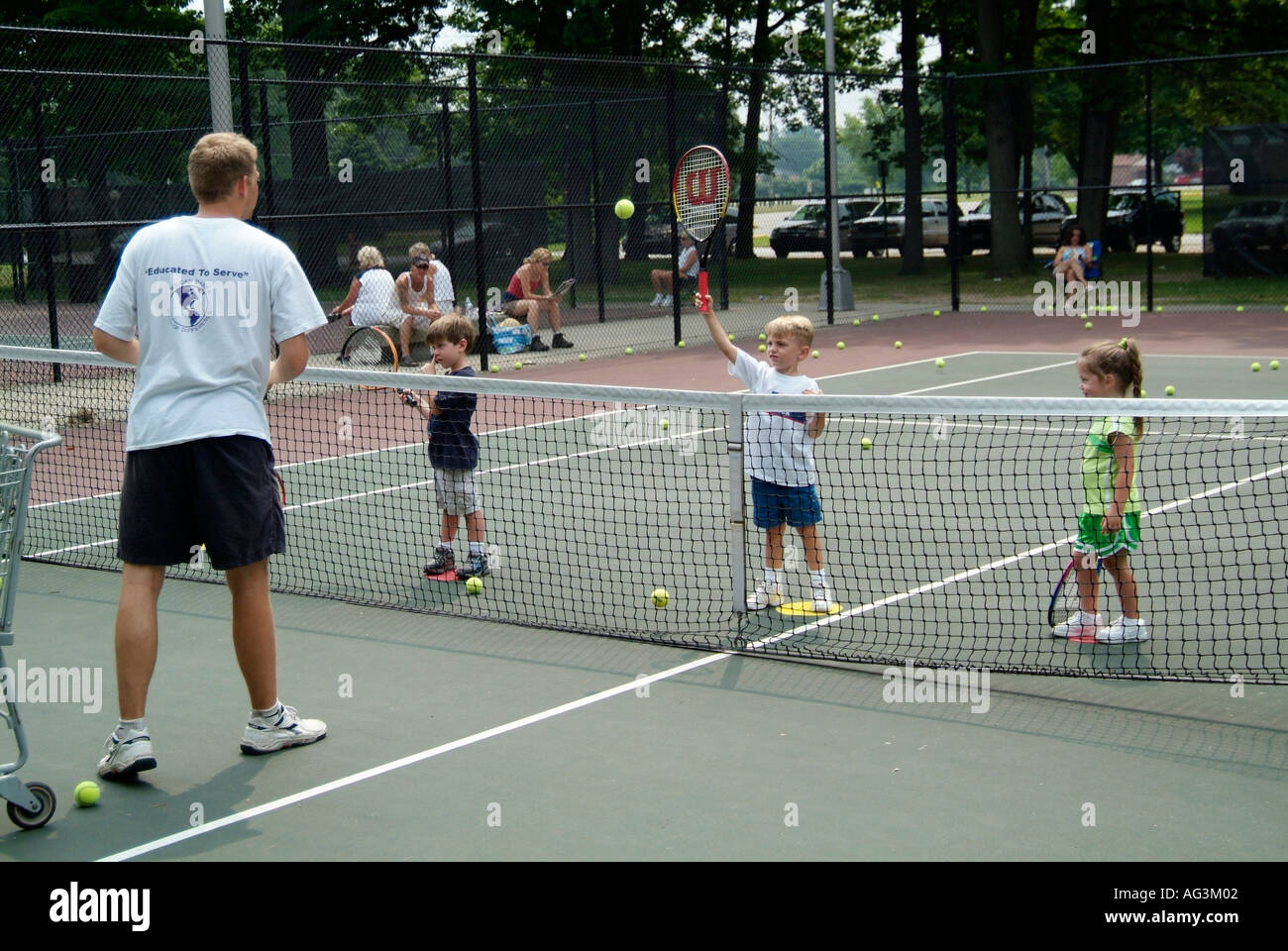 4 and 5 year old children take group tennis lessons taught by college students at a public tennis court Stock Photo