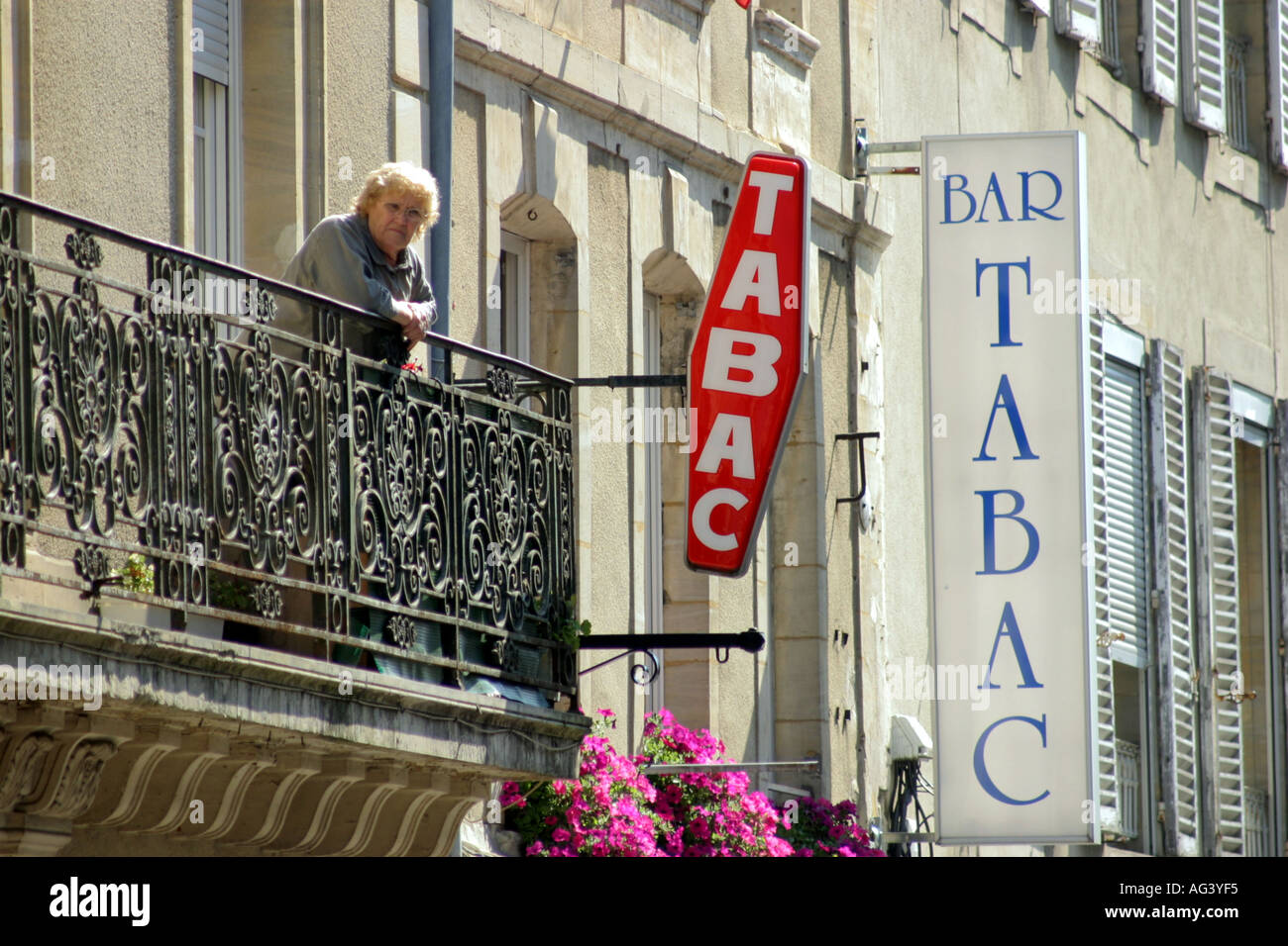 Old woman looking from balcony overlooking street in Bayeux Normandy France Stock Photo