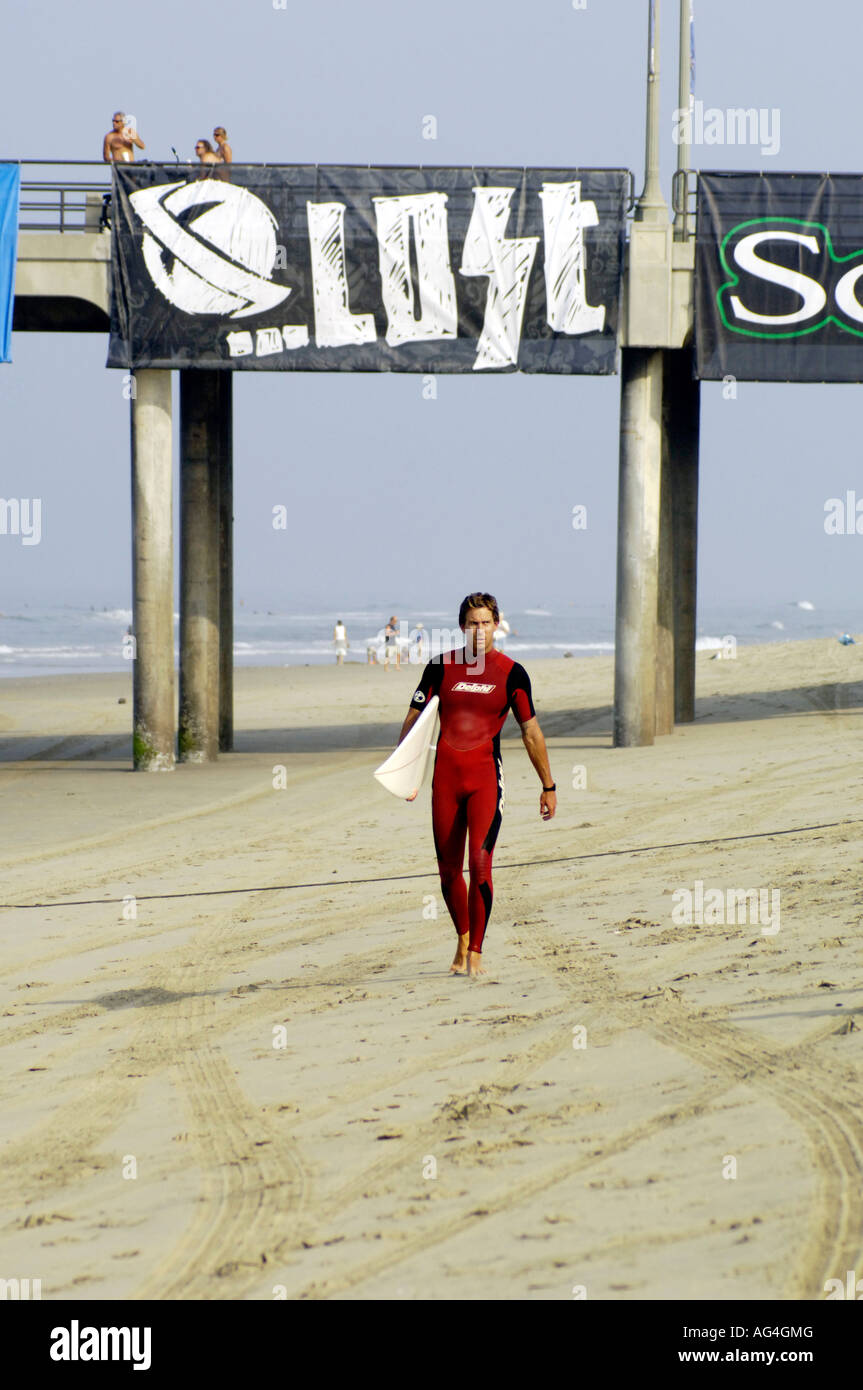 A surfer in a red wetsuit walking on the beach in California Stock