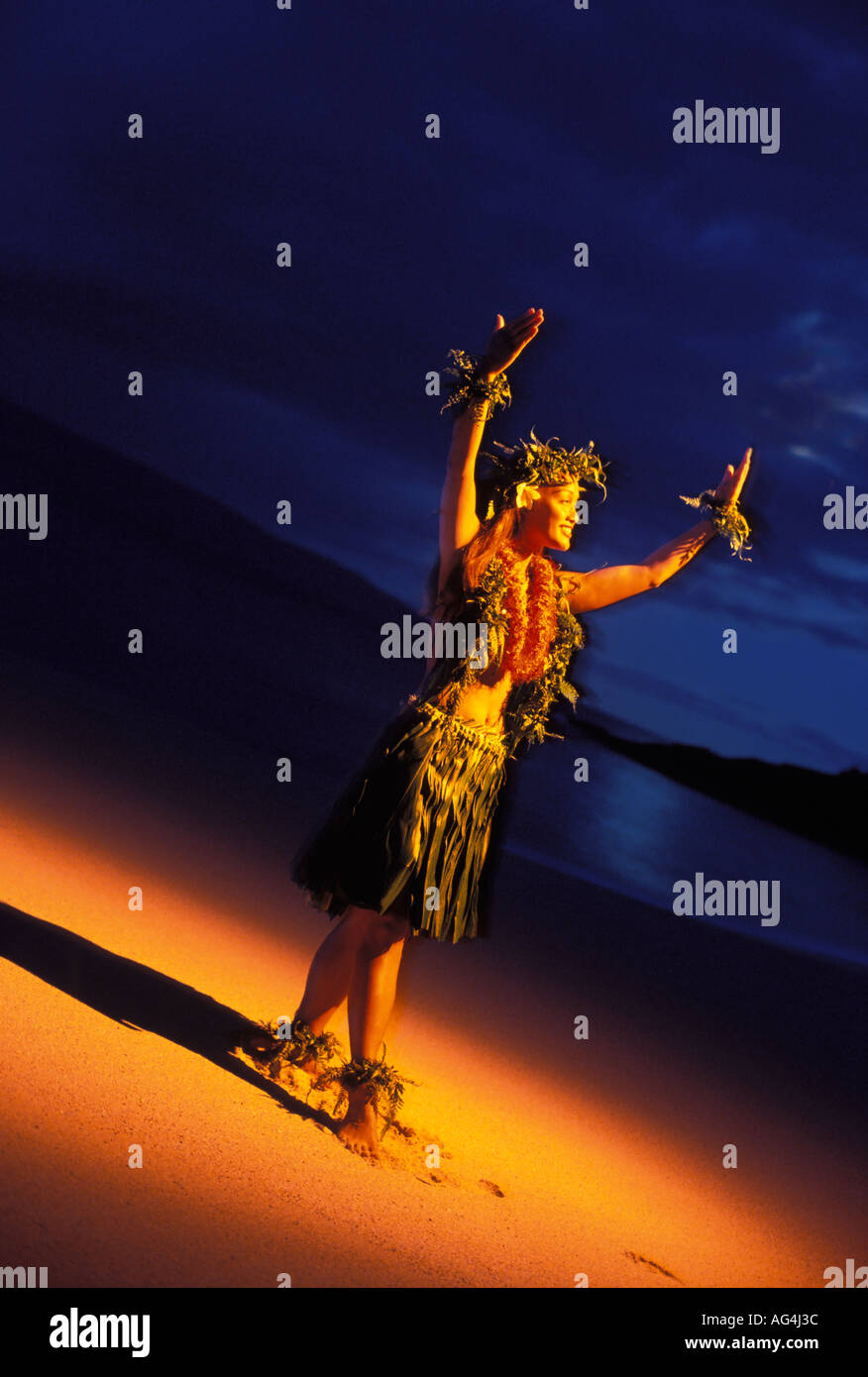 A hula dancer performs at night with a warm glow lighting her body The dancer is in the moon pose at Makena Maui Stock Photo