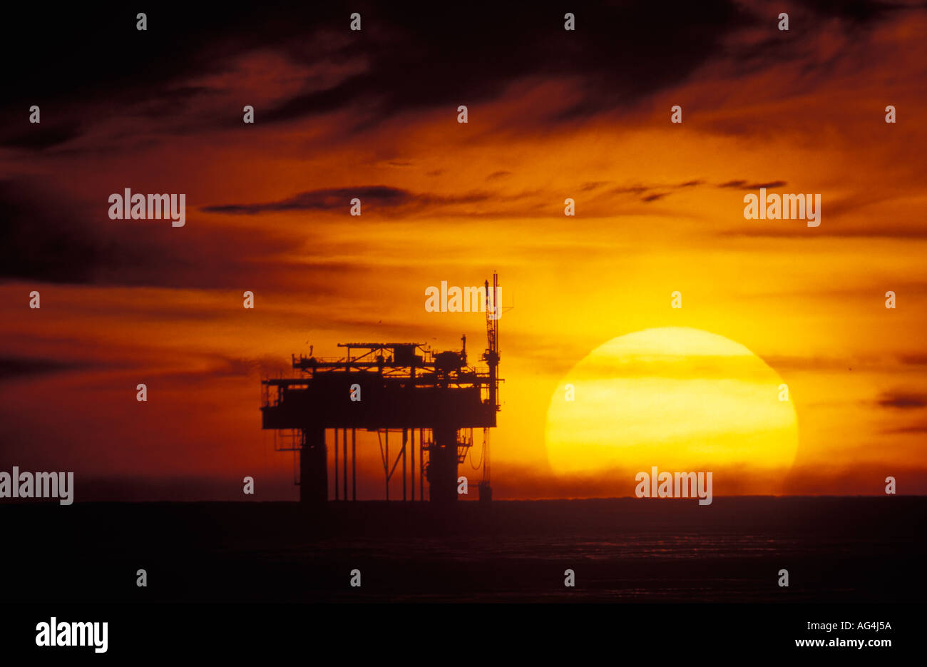 A massive sun sets near a offshore oil rig off the Santa Barbara coastline in Southern California Stock Photo