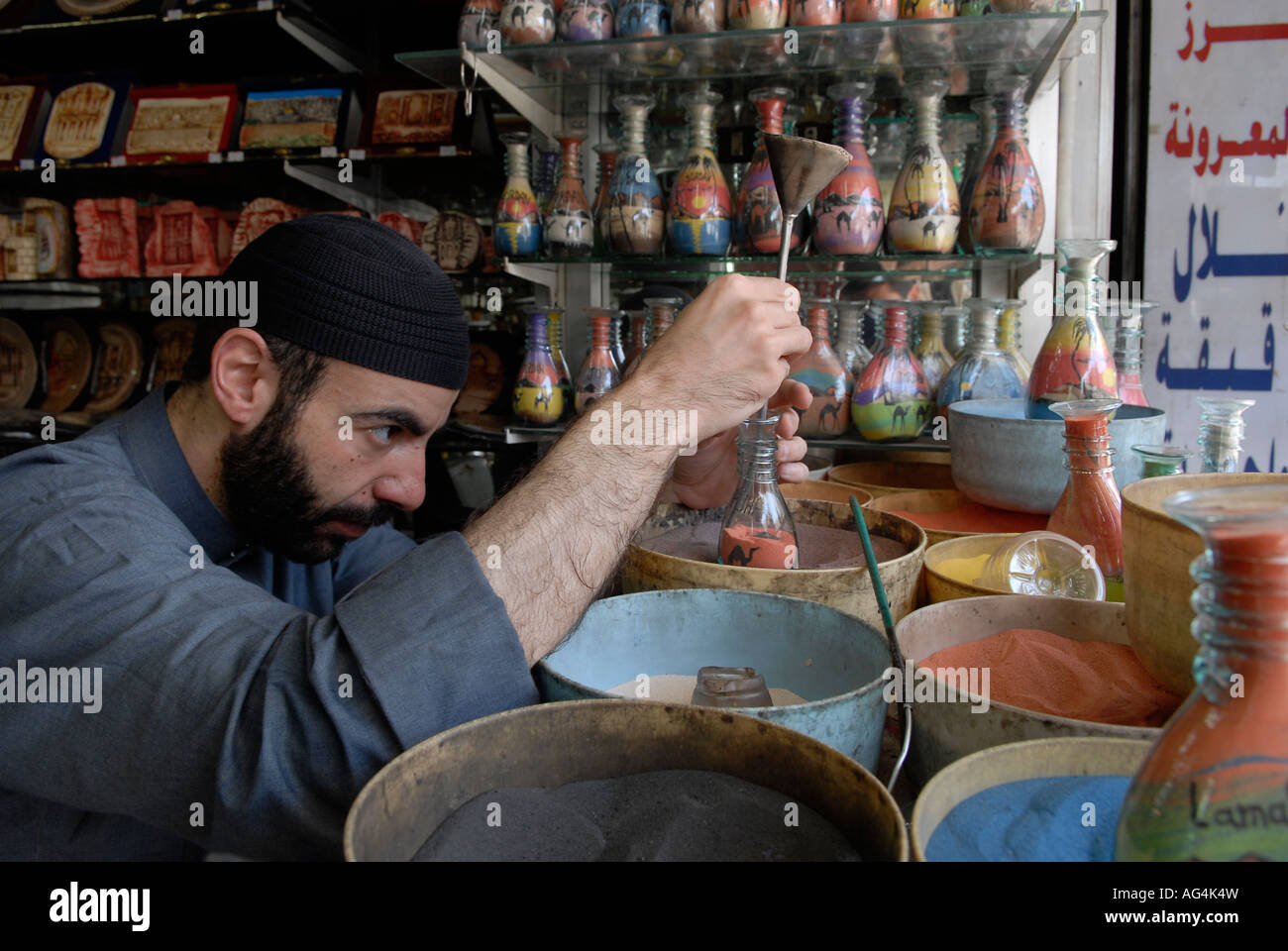 Jordanian man adds colored sand to a decorated bottle filled with multicolored sand rocks that is found in Petra in a souvenir shop in Amman Jordan Stock Photo