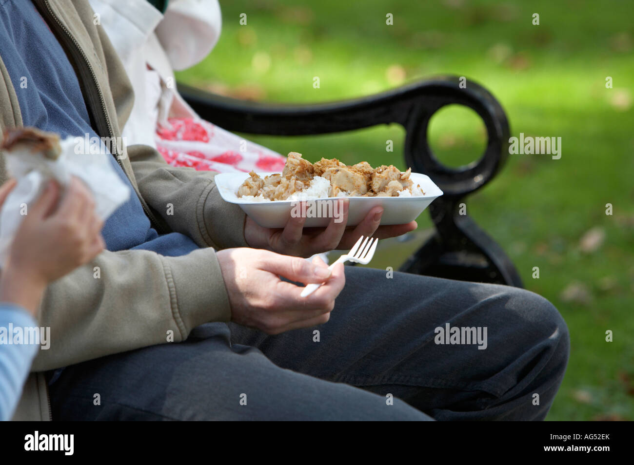 close up of father sitting with two children eating take away chinese meal and crepes outdoors on a park bench Stock Photo