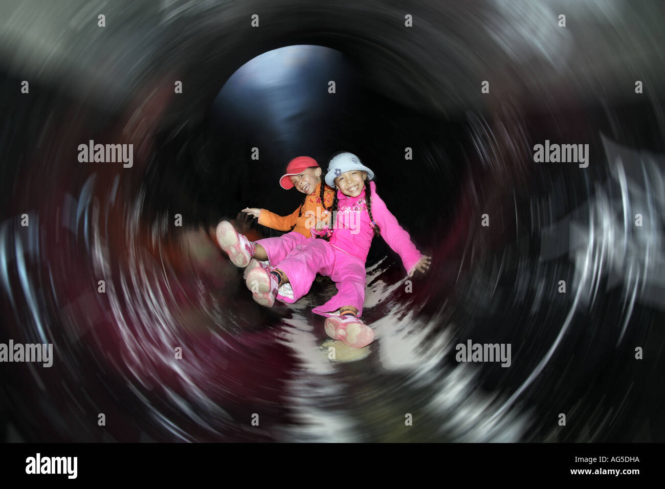 two girls sliding down a pipe Stock Photo