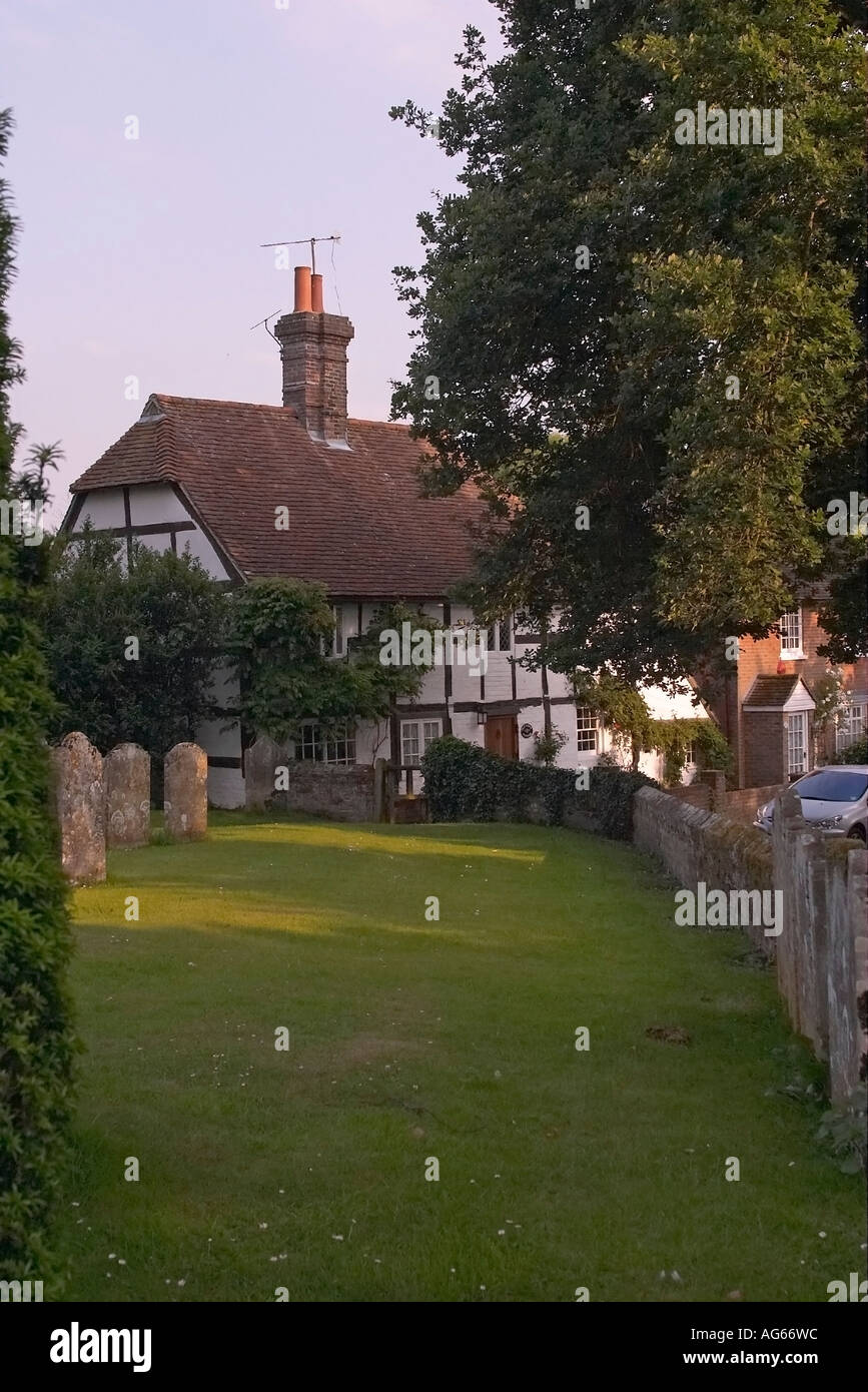 View of traditional thatched cottage through headstones in St Peter's Churchyard, Henfield, Sussex Stock Photo