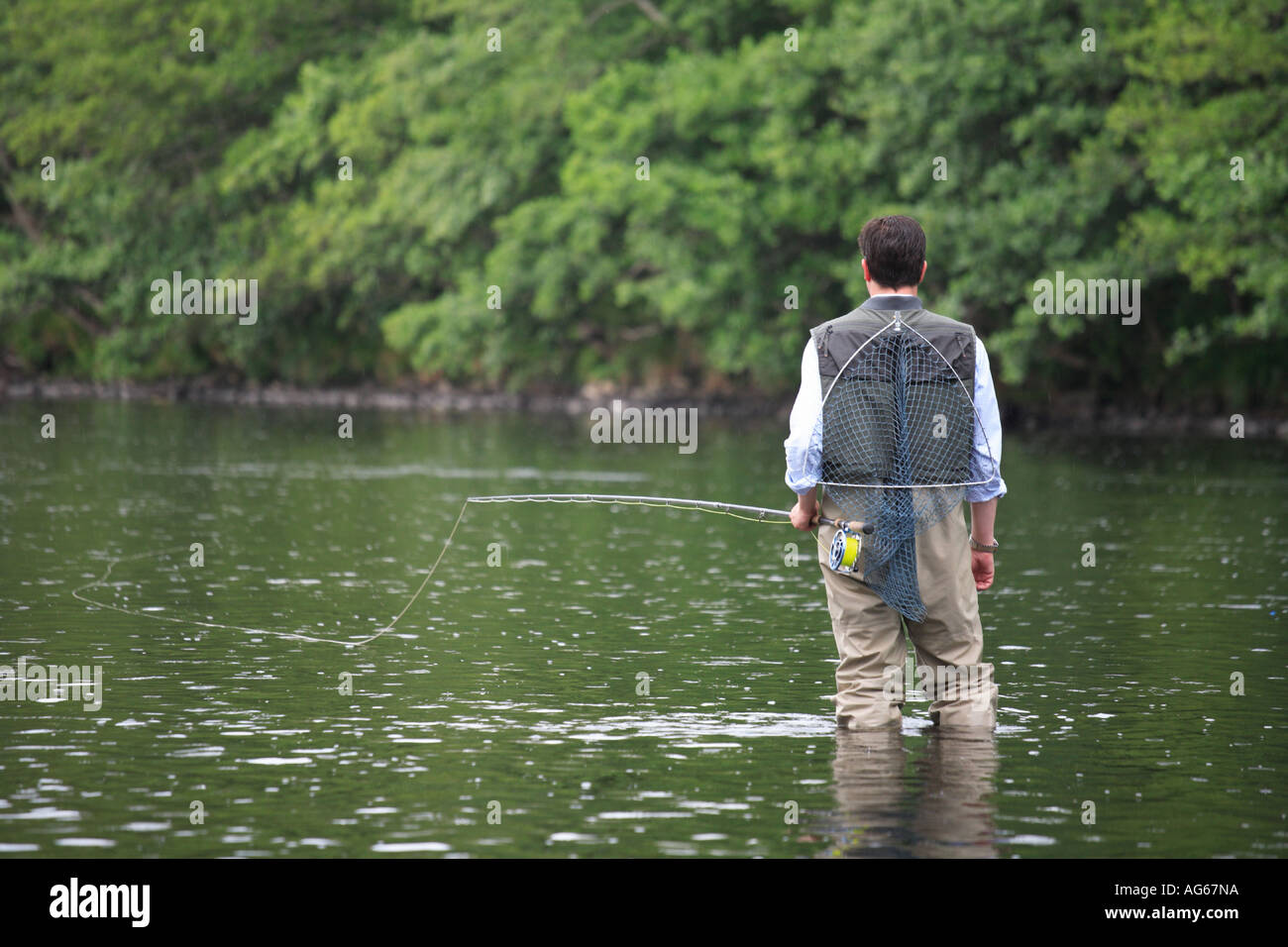 Fly Fisherman in waders, carrying landing net, wading in