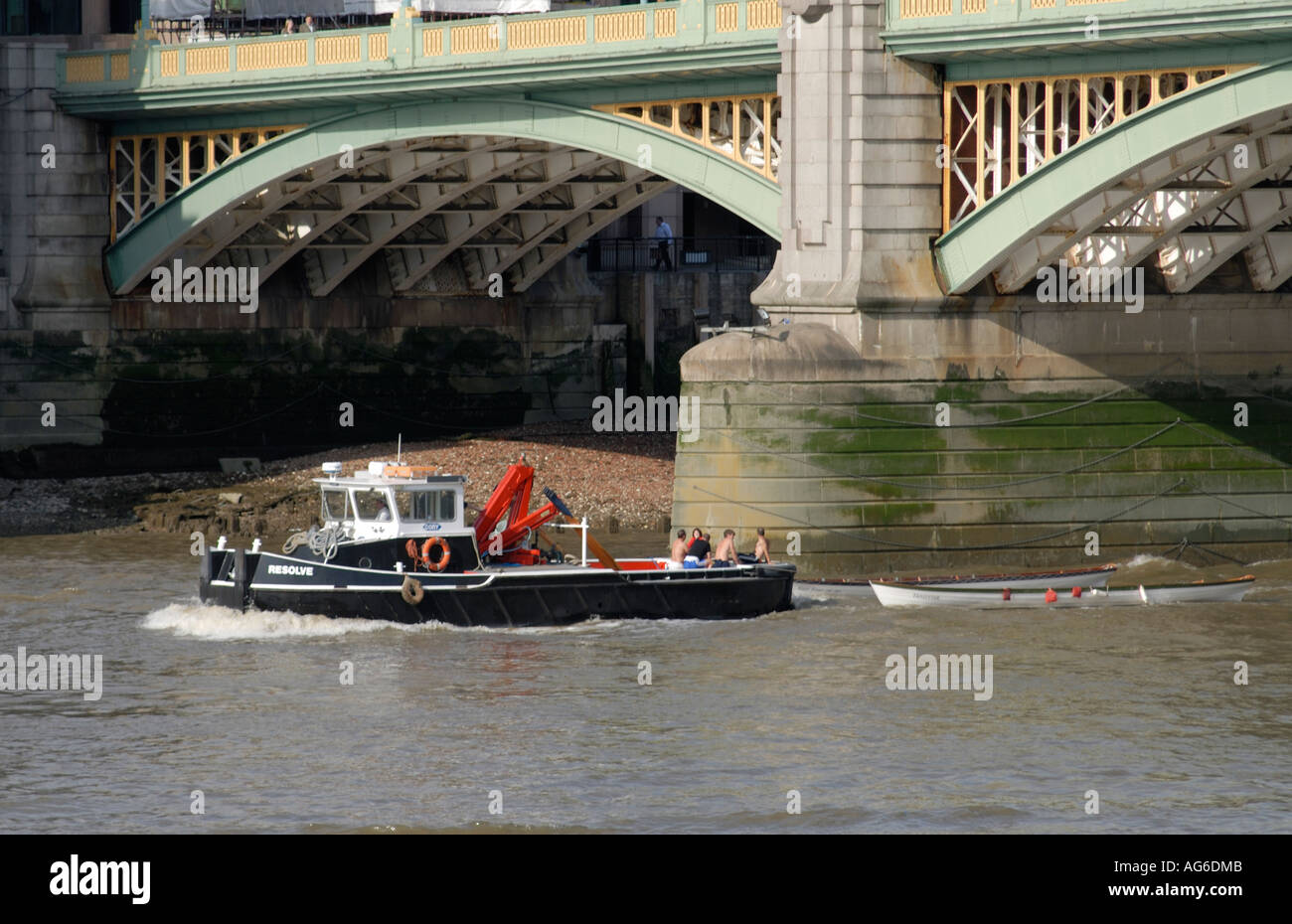 Two white skiffs are towed up the River Thames under Southwark Bridge by the Cory tug Resolve Stock Photo