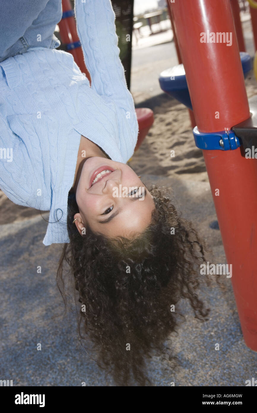 hispanic ten year old girl hanging upside down on playground, smiling Stock Photo