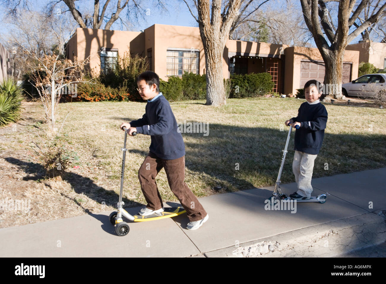 asian boys riding scooters on sidewalk, southwestern united states Stock Photo