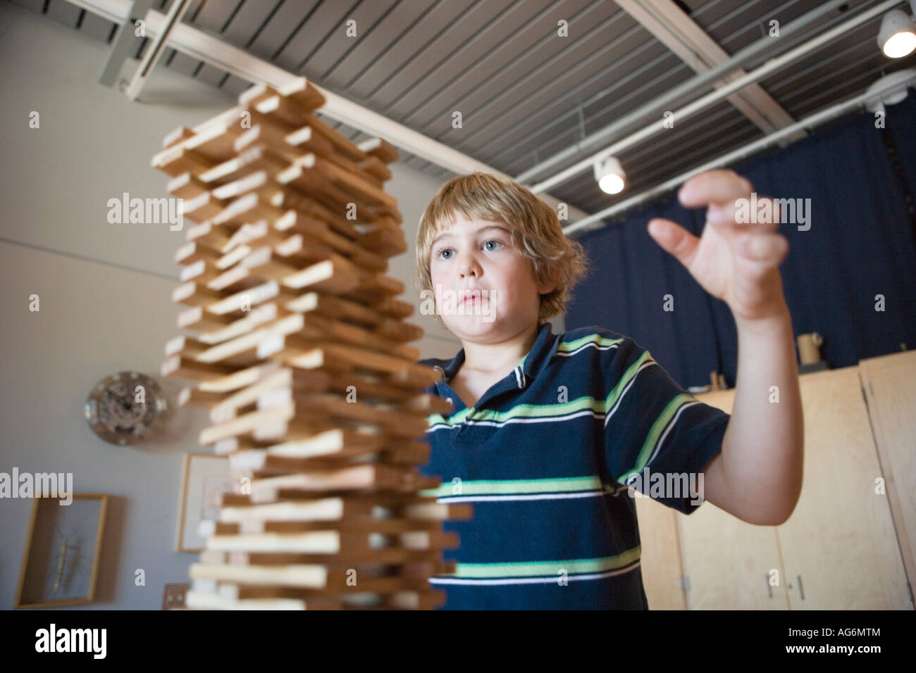 eight year old boy stacking wood blocks as high as he can, watching to make sure they don't topple over Stock Photo