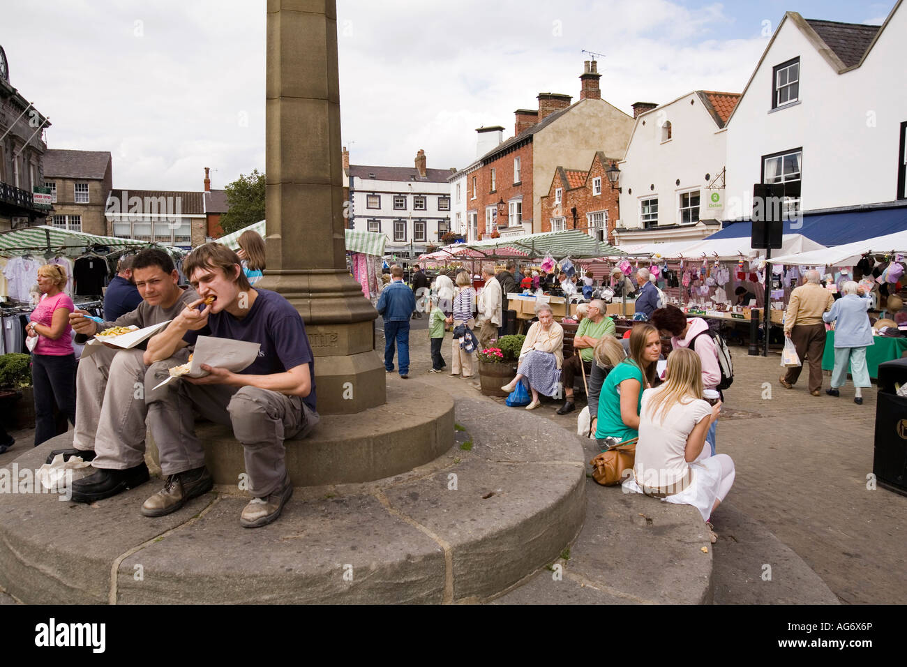 UK Yorkshire Nidderdale Knaresborough market place young people eating fish and chips sat on cross base Stock Photo