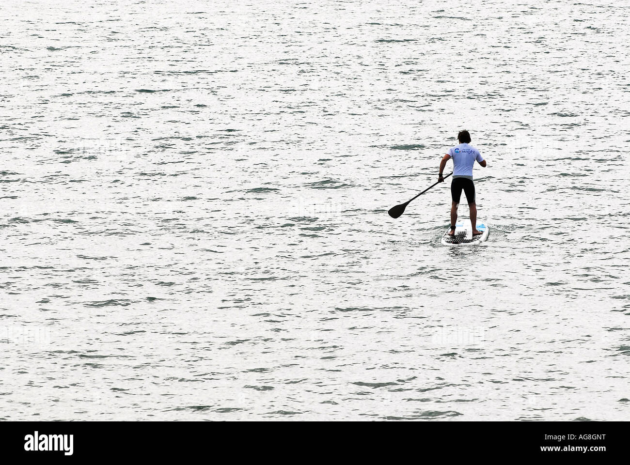 man on surfboard paddling out to sea on a calm day stand up paddle board fitness Stock Photo