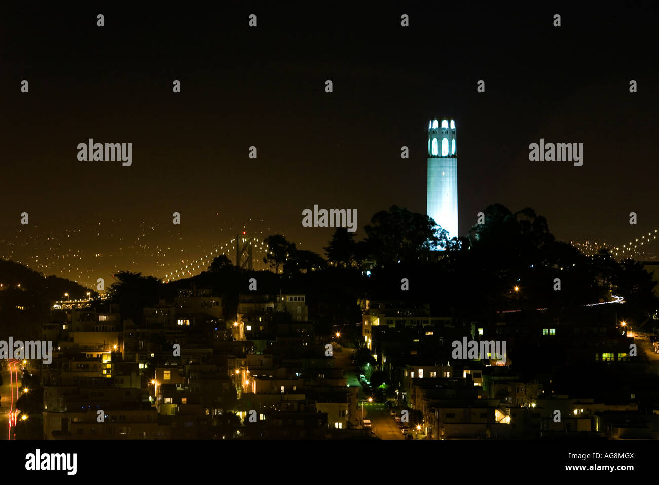 Coit Tower lit at night with the Bay bridge in the background and the homes streets of Telegraph hill in the foreground Stock Photo
