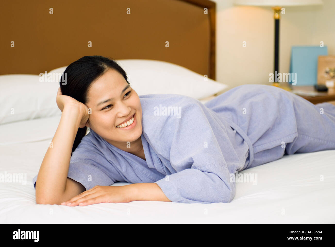 Asian Young Woman Lying On Bed In Hotel Room Watching TV Stock Photo