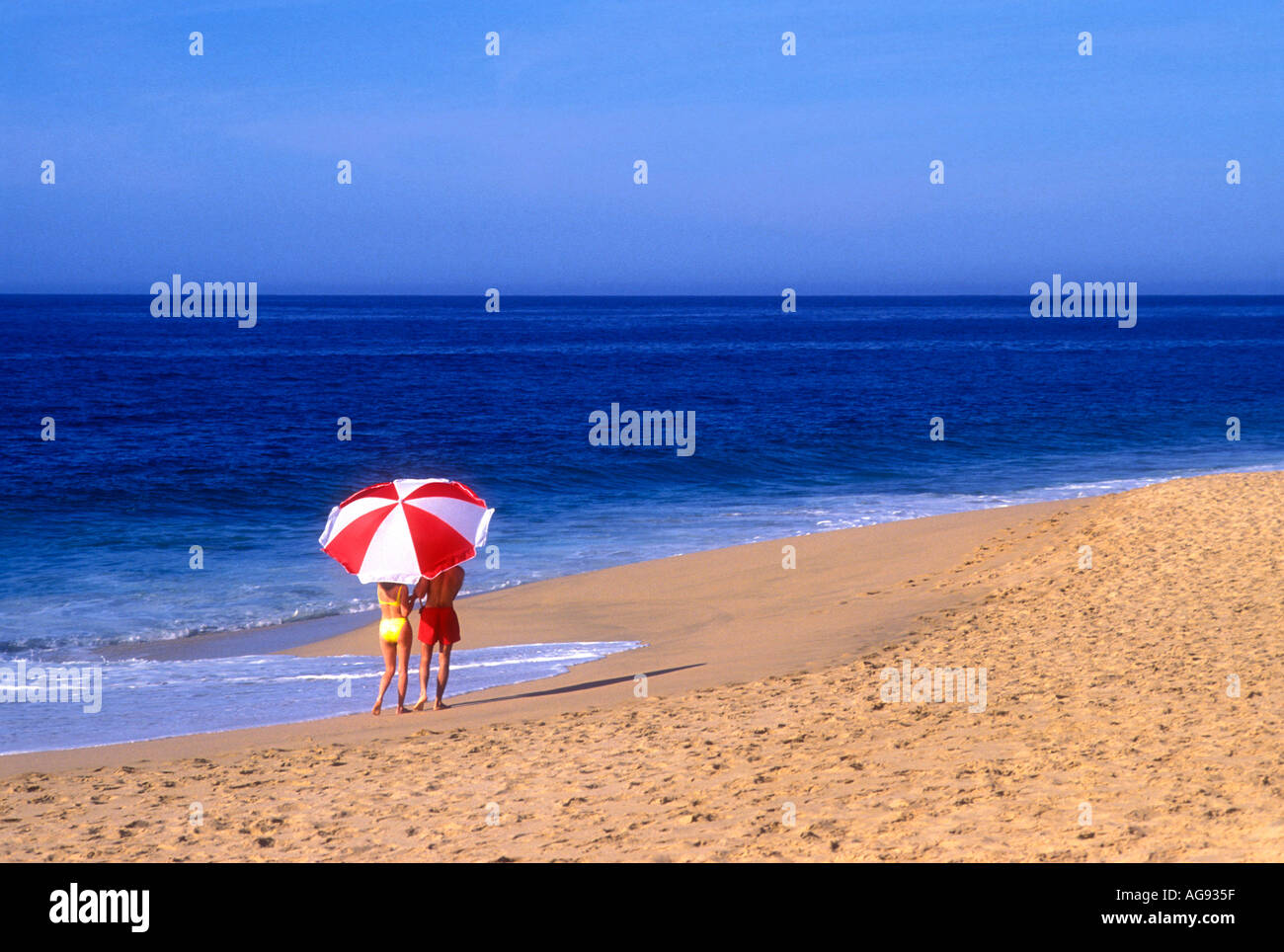 Couple walking along beach under large umbrella in Cabo san Lucas Mexico Model released image Stock Photo