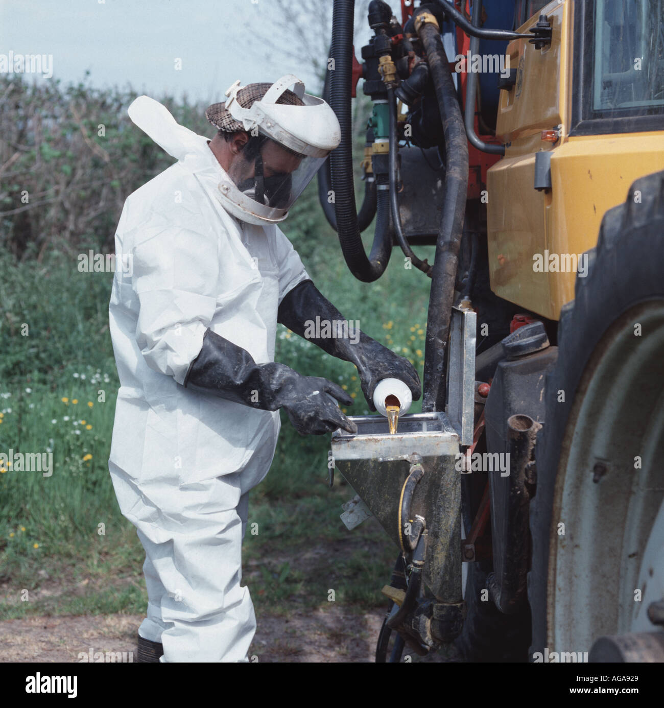 A spray operator in full safety clothing pouring chemical into the spray tank of a Gem sprayer mounted on a JCB Fastrac tractor Stock Photo