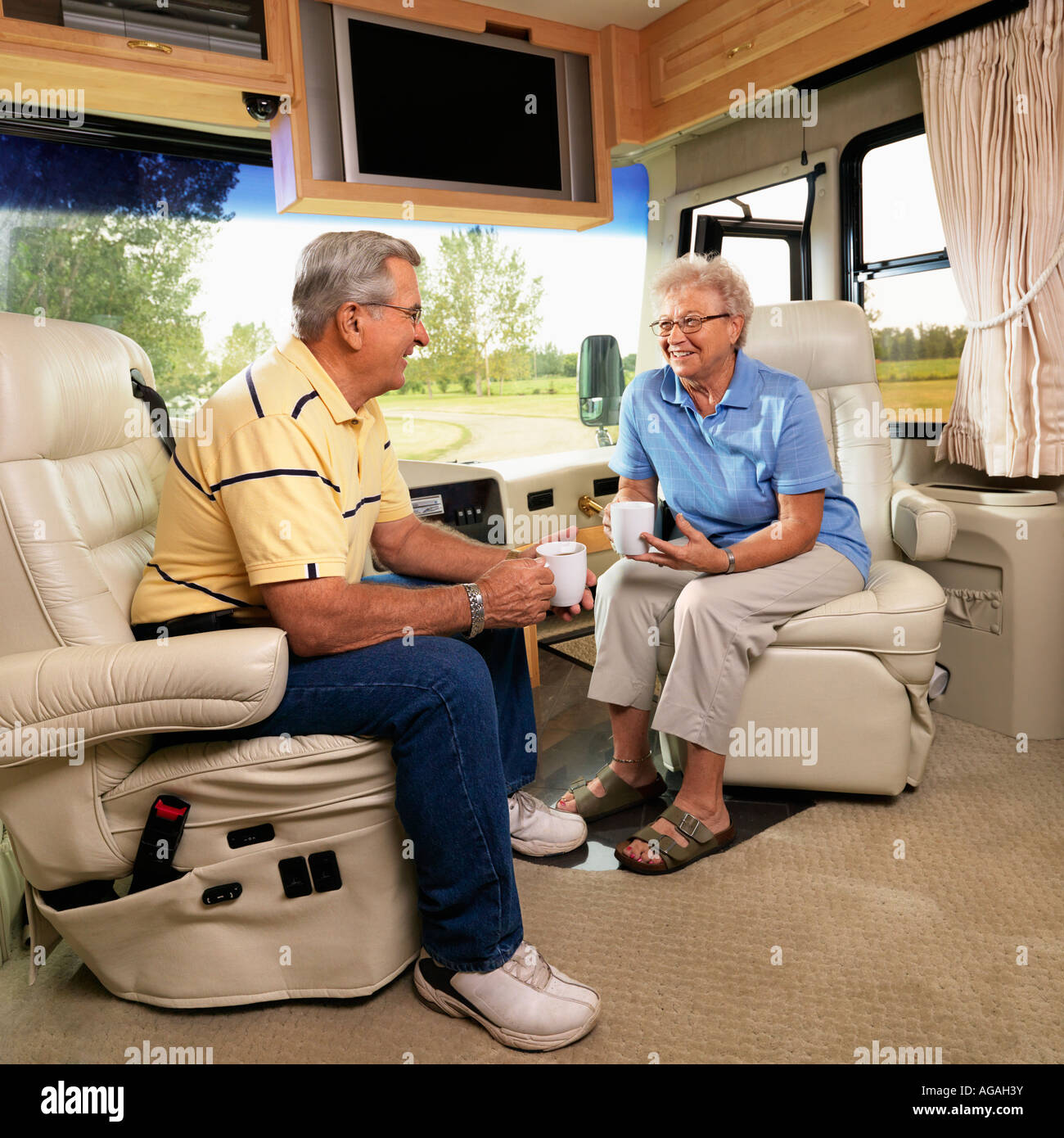 Senior couple sitting in RV holding coffee cups and smiling Stock Photo