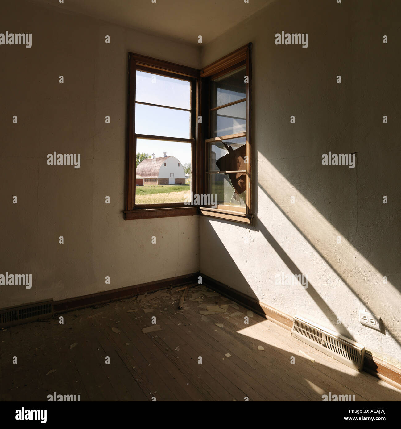 Dark empty abandoned room with sunrays stretching across wall from corner window Stock Photo