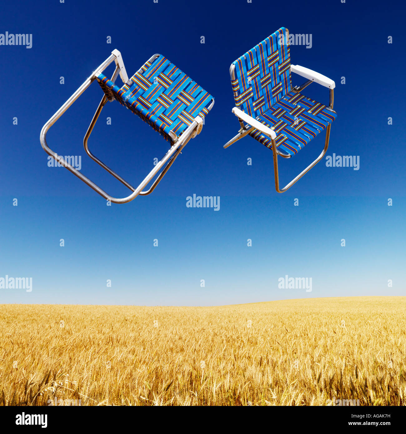 Two lawn chairs in mid air above a field of wheat with blue sky Stock Photo