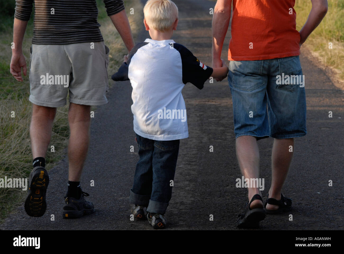 Rear view of two men and a boy walking together and holding hands down ...