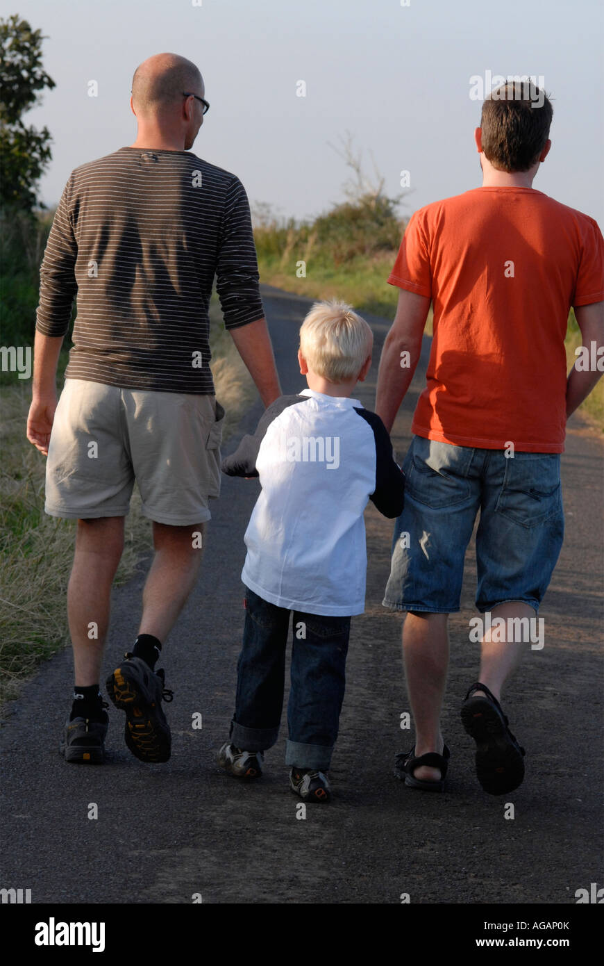 Rear view of two men and a boy walking together and holding hands down ...