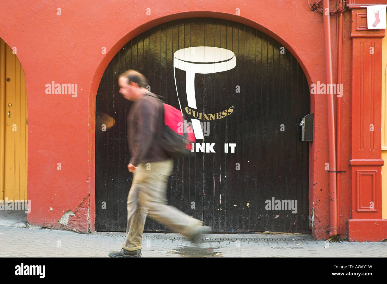A man walks past a door a advertising Guiness beer in Kilkenny, Ireland. Stock Photo