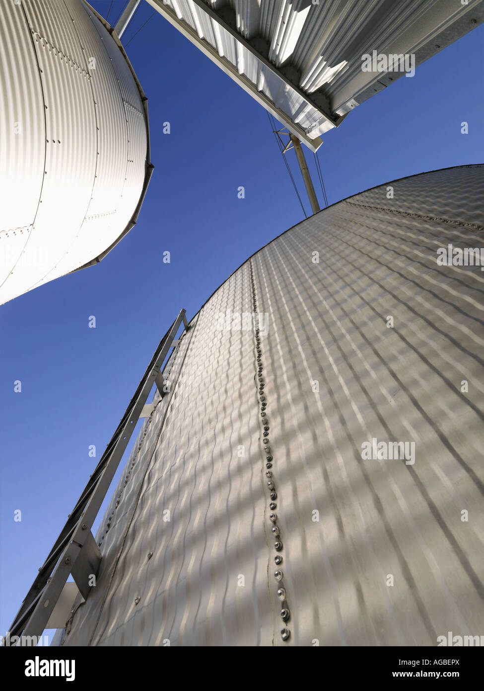 Low angle view of metal grain storage silos against blue sky Stock Photo