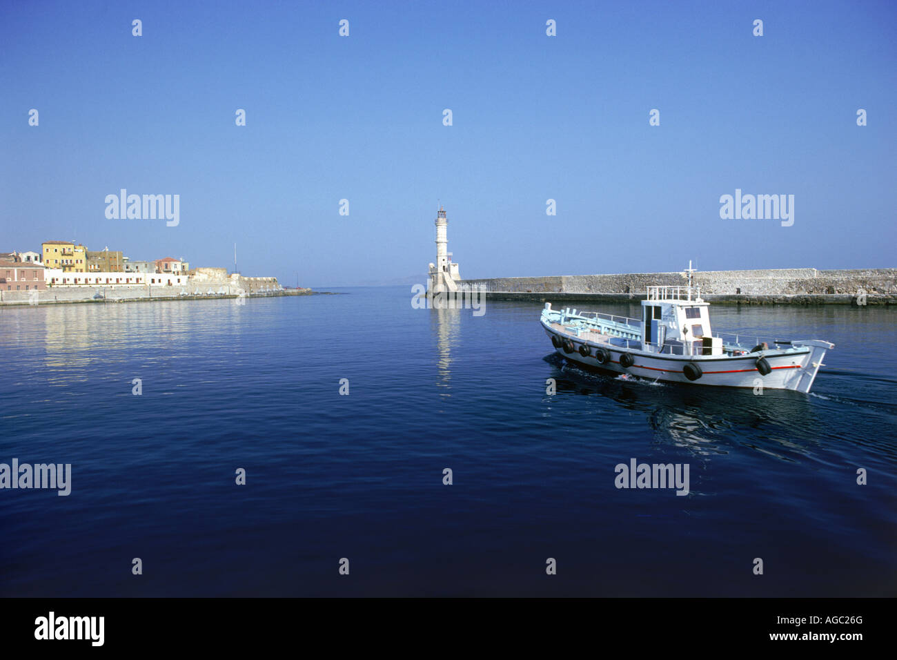 Fishing boat leaving for Mediterranean Sea from port town of Chania (Xhania) with lighthouse on north coast of Crete Stock Photo
