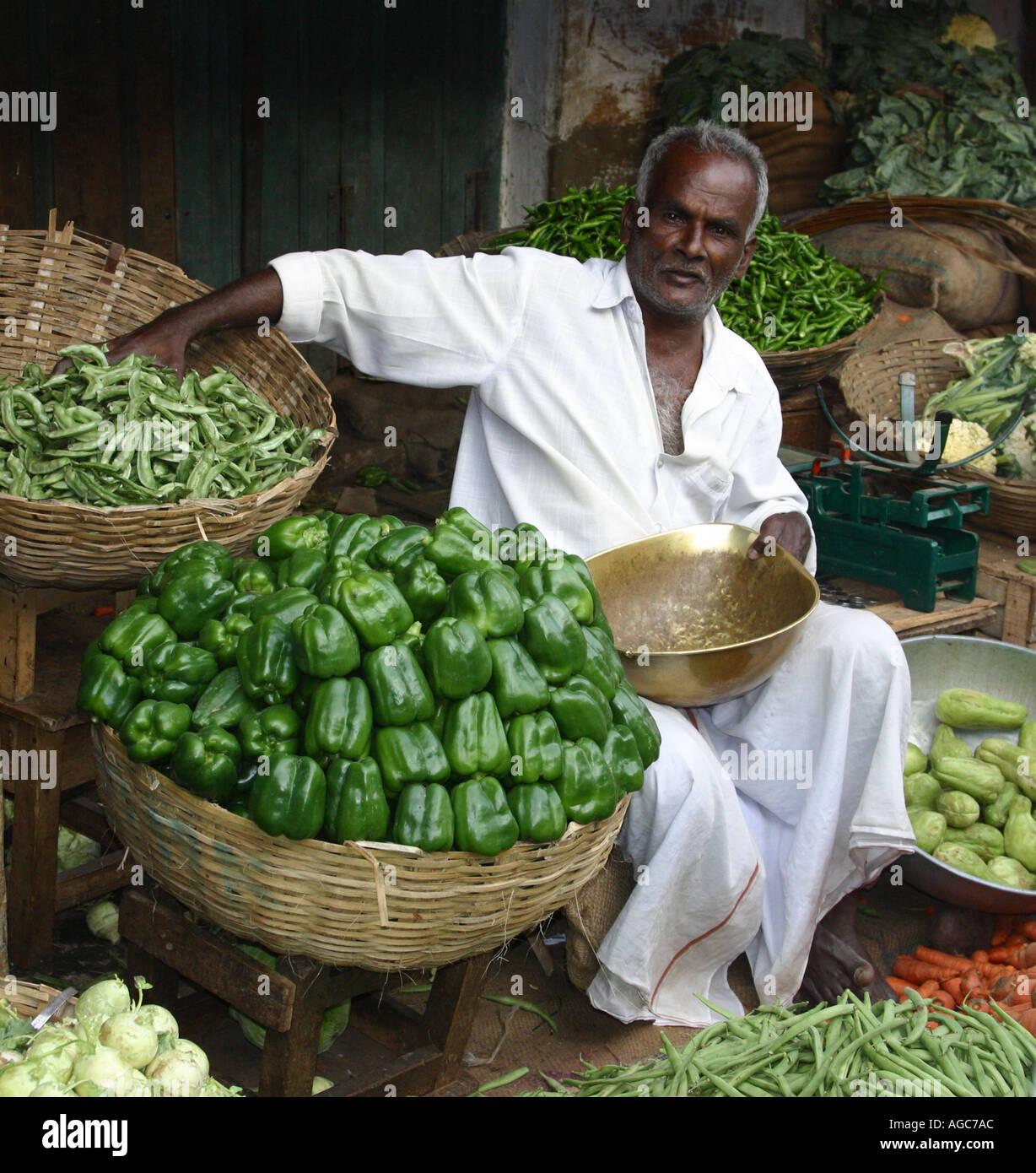 Indian vegetable seller trading at market with Green peppers and okra Stock Photo