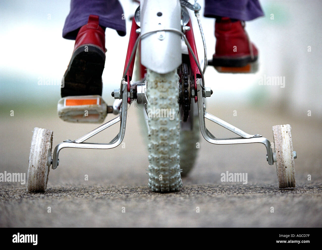Young child on a bicycle with stabilizers or stabilisers or training wheels Stock Photo