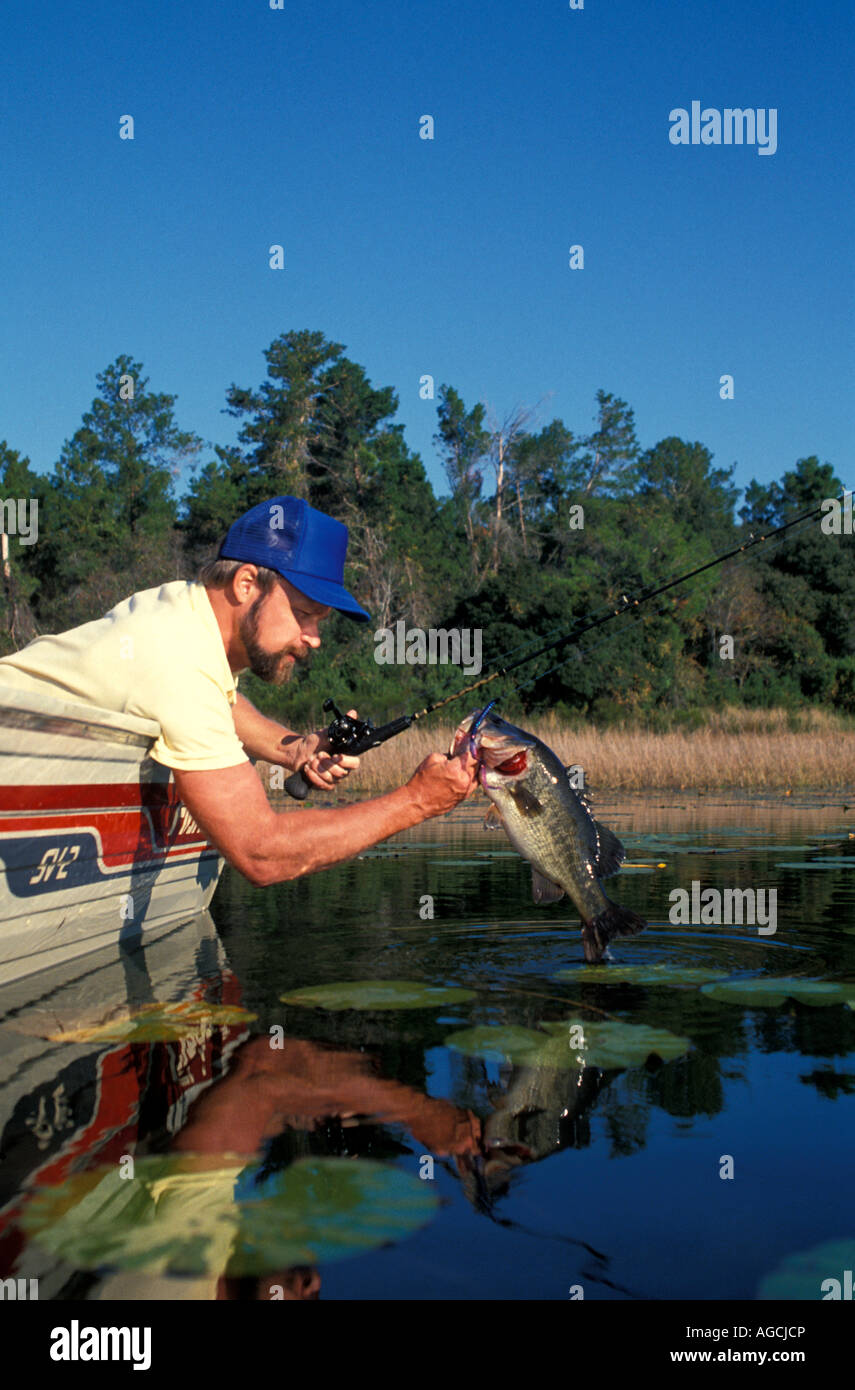Angler leaning over boat holding trophy largemouth bass Stock Photo