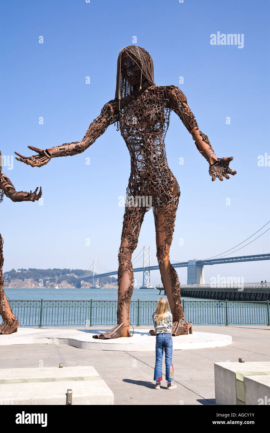 Girl looking a metal sculpture with Oakland Bay Bridge in background, San Francisco, CA USA Stock Photo