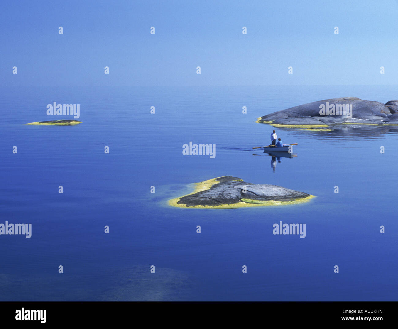 Couple in tiny rowboat between small rocky islands amid 30,000 island Stockholm Archipelago in Baltic Sea Stock Photo