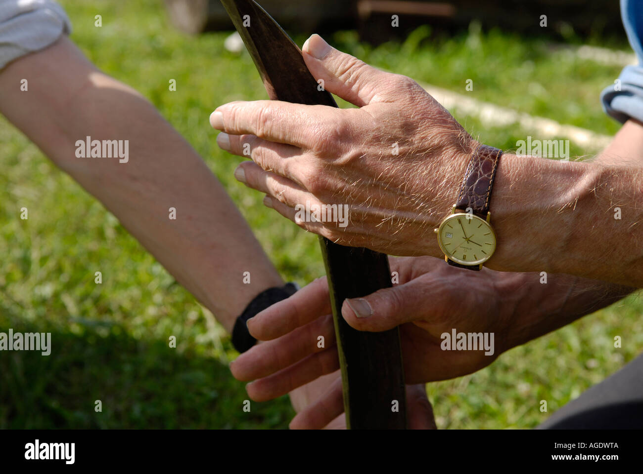Stock image of a man using a wetstone to sharpen a scythe blade while cutting a field of hay in New Brunswick Canada Stock Photo