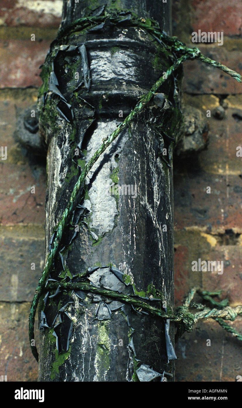 Old and delapidated exterior waste pipe with aged green string tied around it. Stock Photo