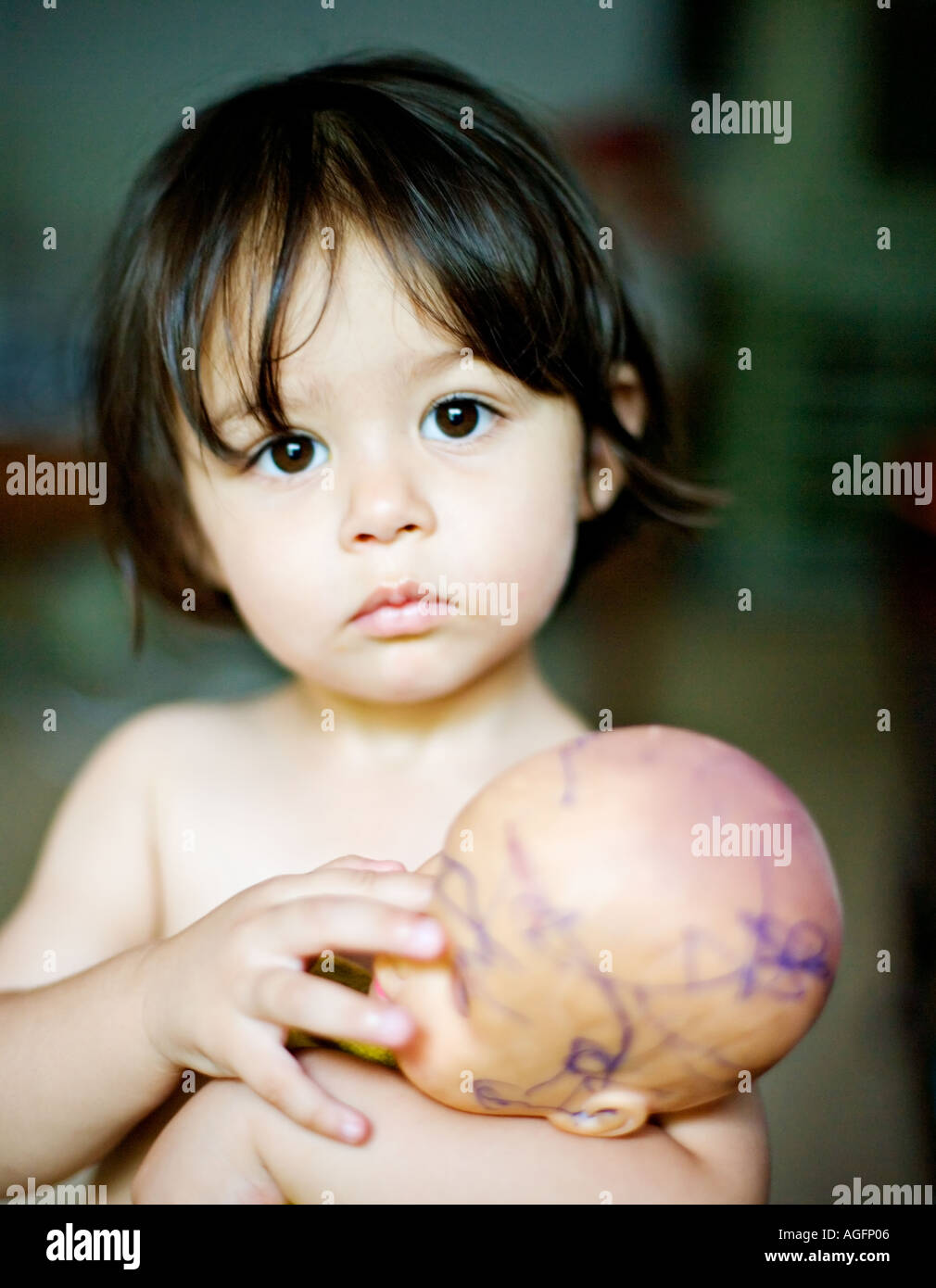 Cute Little Girl With Doll And Dark Brown Hair Looks Straight Into