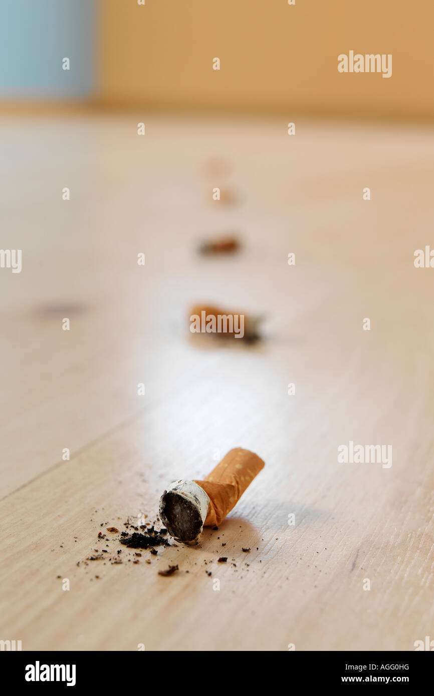 Close up of Cigarette Bud on Wooded Floor of an empty room Last of a line  of cigarette buds fading in the unfocused background Stock Photo