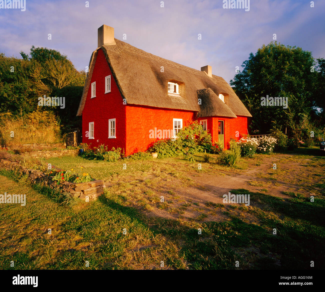 a red painted cottage with a thatched roof in a rural countryside setting Stock Photo